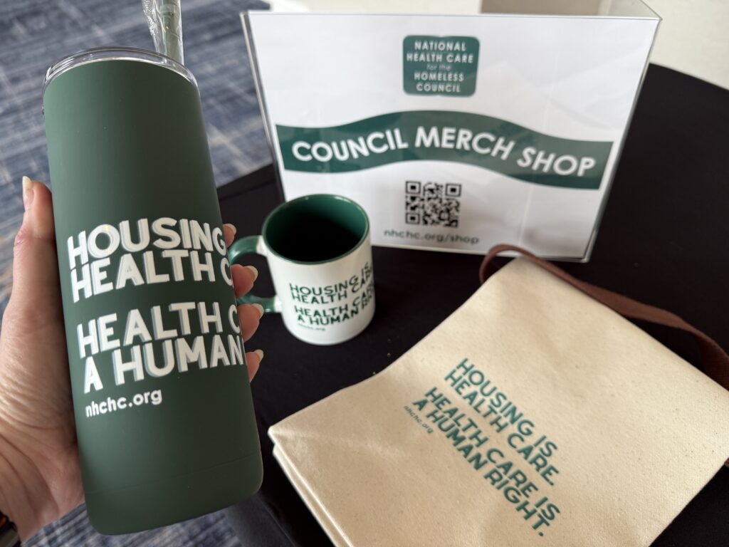 A hand holding a large drink tumbler and some other merch for NHCHC.