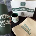 a hand holds a drink tumbler in front of other merch